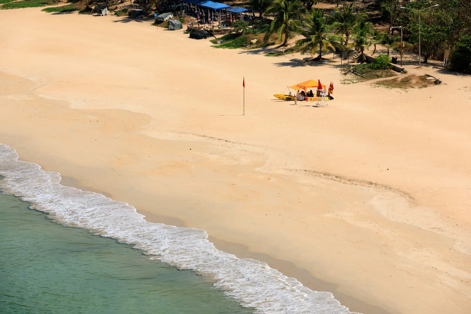 Kamala Beach in Phuket, Thailand, with a wide sandy shoreline, gentle waves, palm trees, and a lifeguard station.