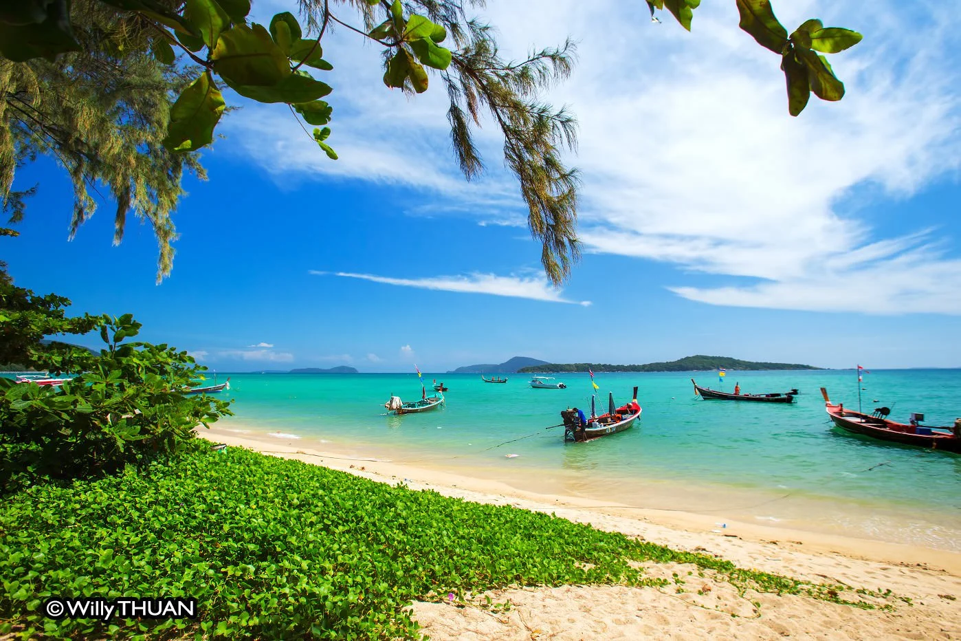 Rawai Beach in southern Phuket with traditional longtail boats anchored in turquoise water along the tropical shoreline.