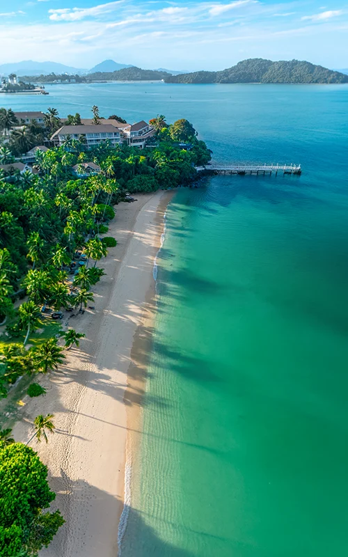Aerial view of Cape Panwa in Phuket, Thailand, with a quiet sandy beach, turquoise sea, tropical greenery, and a private pier.
