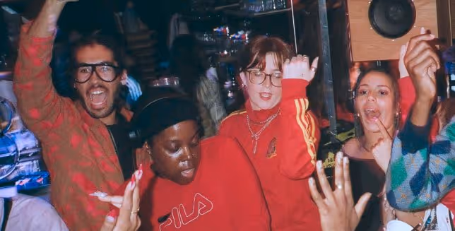Group of people dancing and posing energetically in a colorful indoor setting.