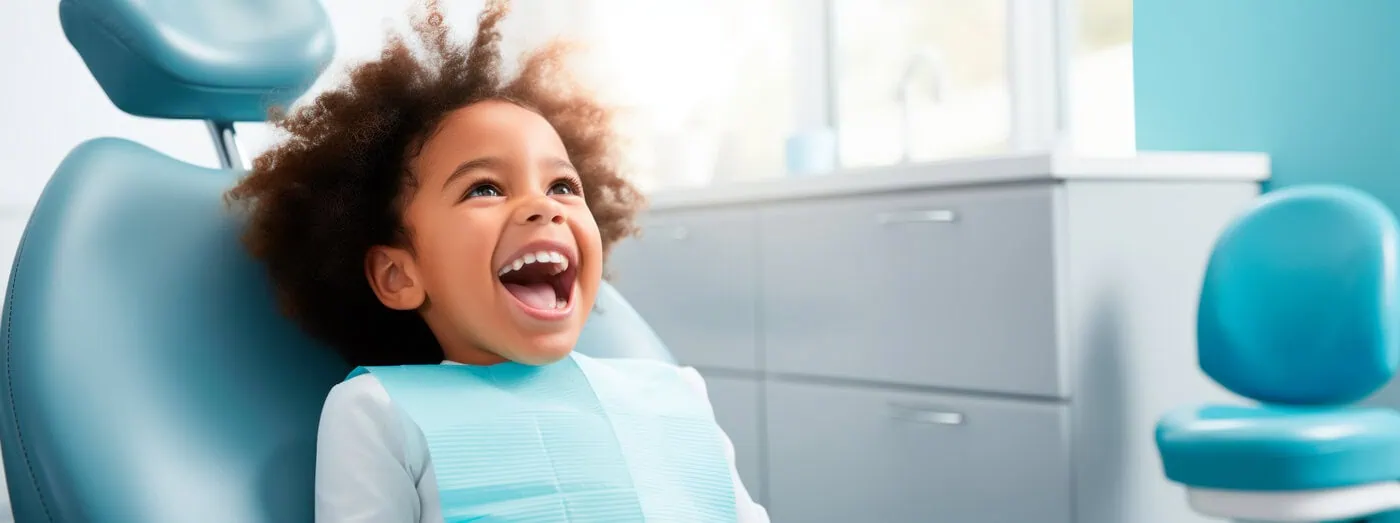 Happy young child sitting in a dental chair with mouth open, wearing a dental bib in a bright clinic.