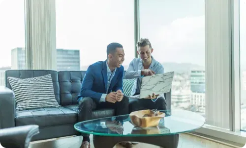 Two men discussing work while looking at a laptop in office lounge.