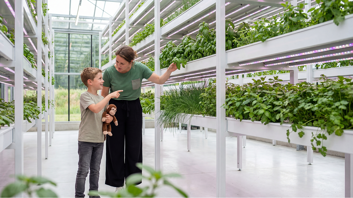 Woman and boy with a stuffed monkey exploring plants in a bright indoor vertical garden.