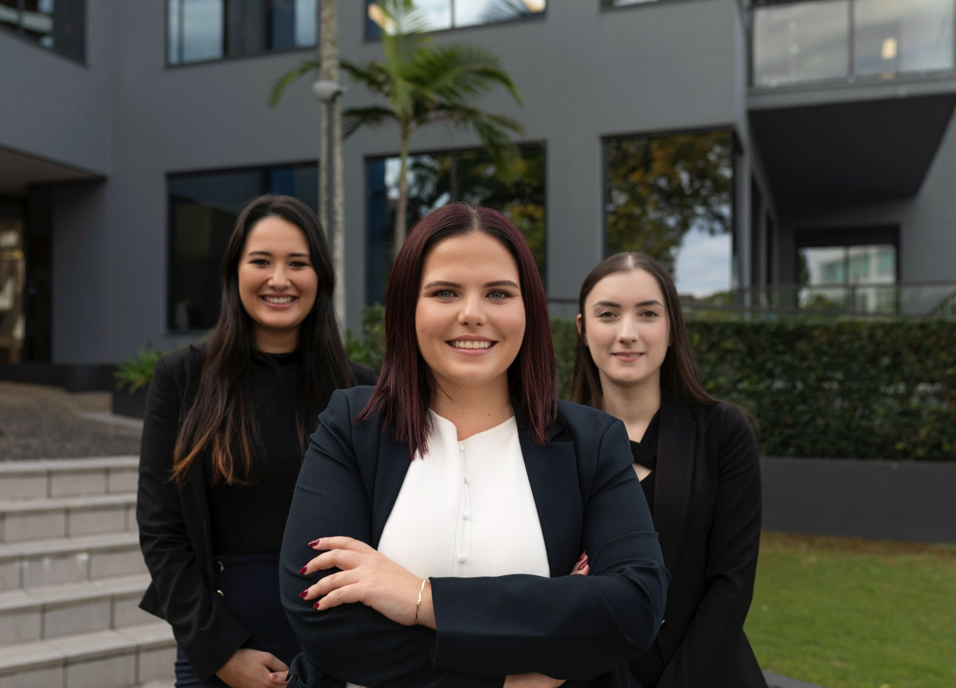 Three professional women smiling in front of a corporate office building.
