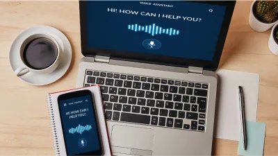 Laptop und Smartphone mit Sprachassistent-Interface auf Schreibtisch.