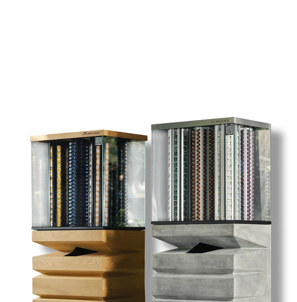 Two Meama Droppers machines with transparent display cases filled with colorful coffee capsules and sculpted geometric bases