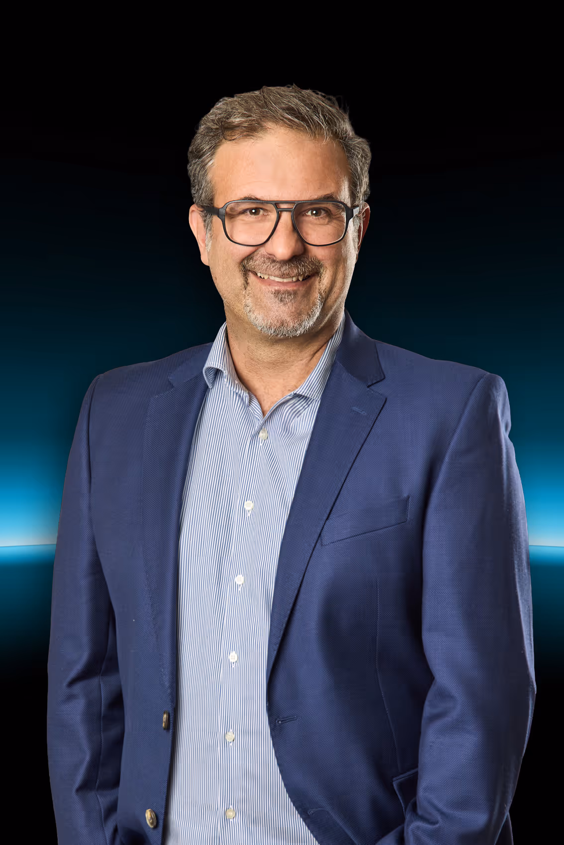 Männlicher Geschäftsmann mit Brille, grauem Bart und blauem Anzug vor dunklem Hintergrund mit blauem Licht.