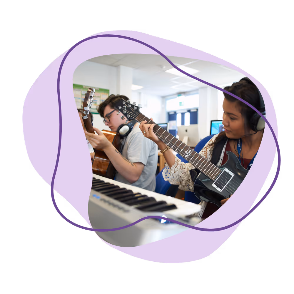 Two students wearing headphones play electric and acoustic guitars in a music class.