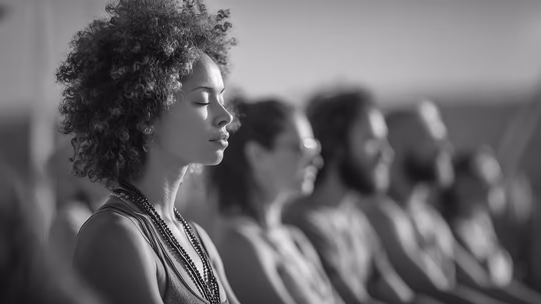 Profile of a woman with curly hair and closed eyes meditating in a group setting.