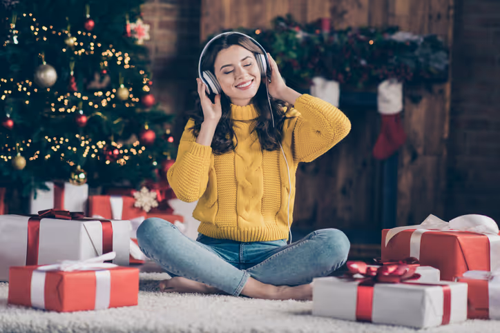 Girl with headphones on sitting in front of a christmas tree surrounded by presents