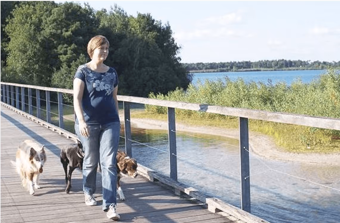 Zwei Menschen mit Hund auf Holzweg am Wasser