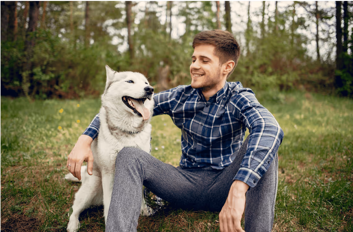 Mann mit Hund im Grünen, sitzt auf Holzbank