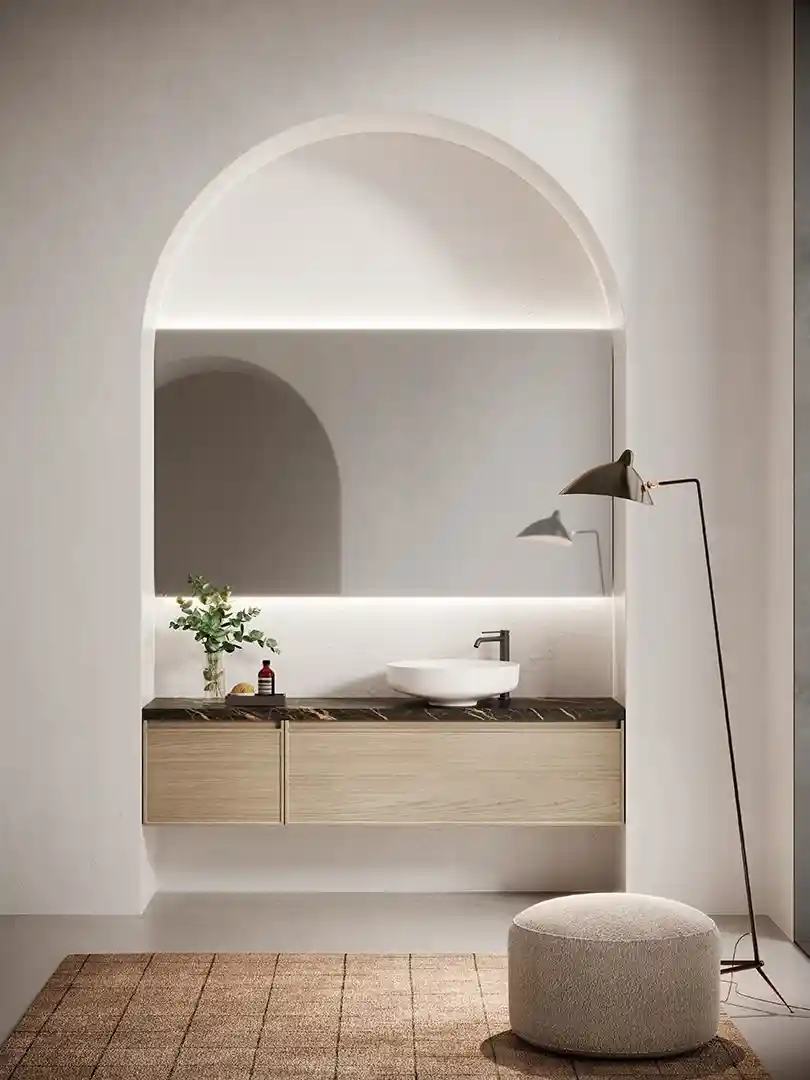 Minimalist bathroom vanity with a large rectangular mirror inset into an arched niche, black marble countertop, white vessel sink, and a modern floor lamp beside a round beige pouf on a textured rug.