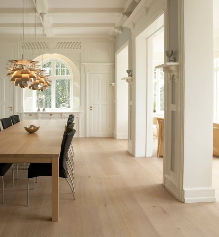 Stack of three decorative cushions with abstract multicolored patterns on a cream textured sofa against a muted pink wall.