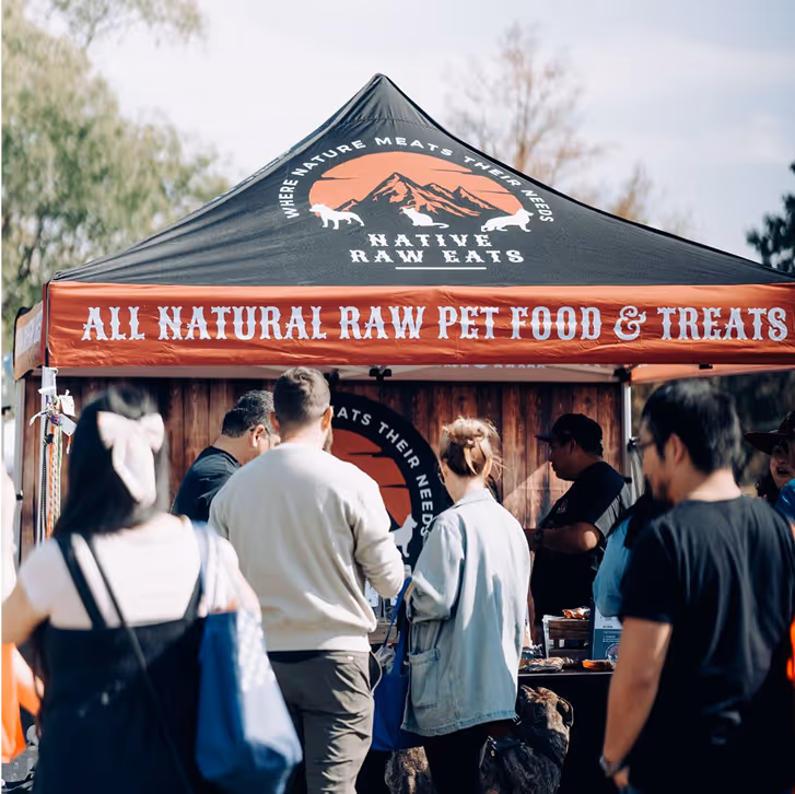 Group of people standing in front of a Native Raw Eats tent offering all natural raw pet food and treats.