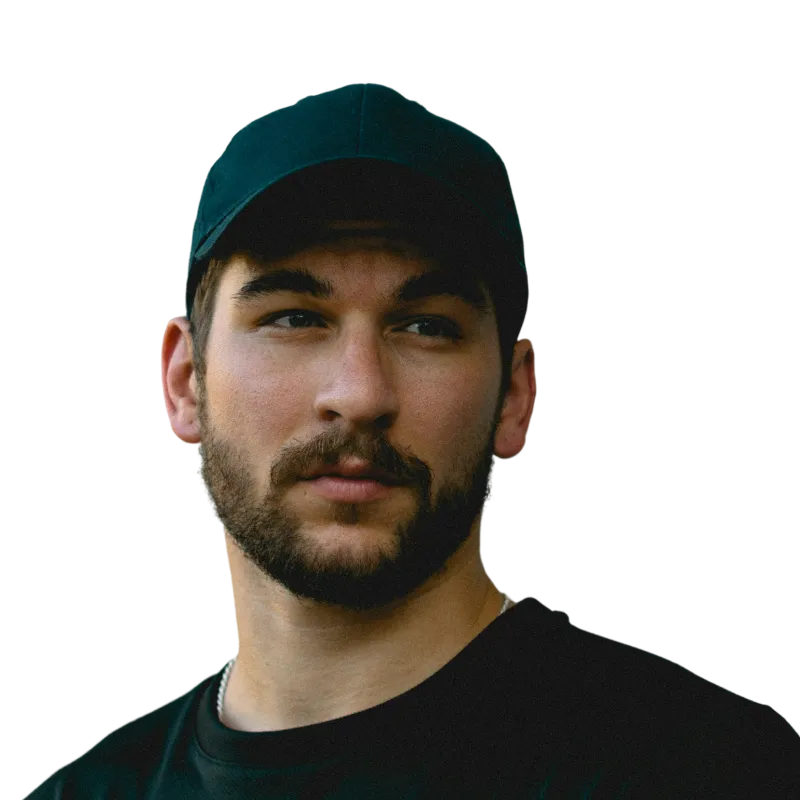 Young man with a beard wearing a black cap and black shirt looking slightly to the side.