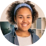 Smiling young woman with curly hair wearing a blue headband and casual clothing indoors.