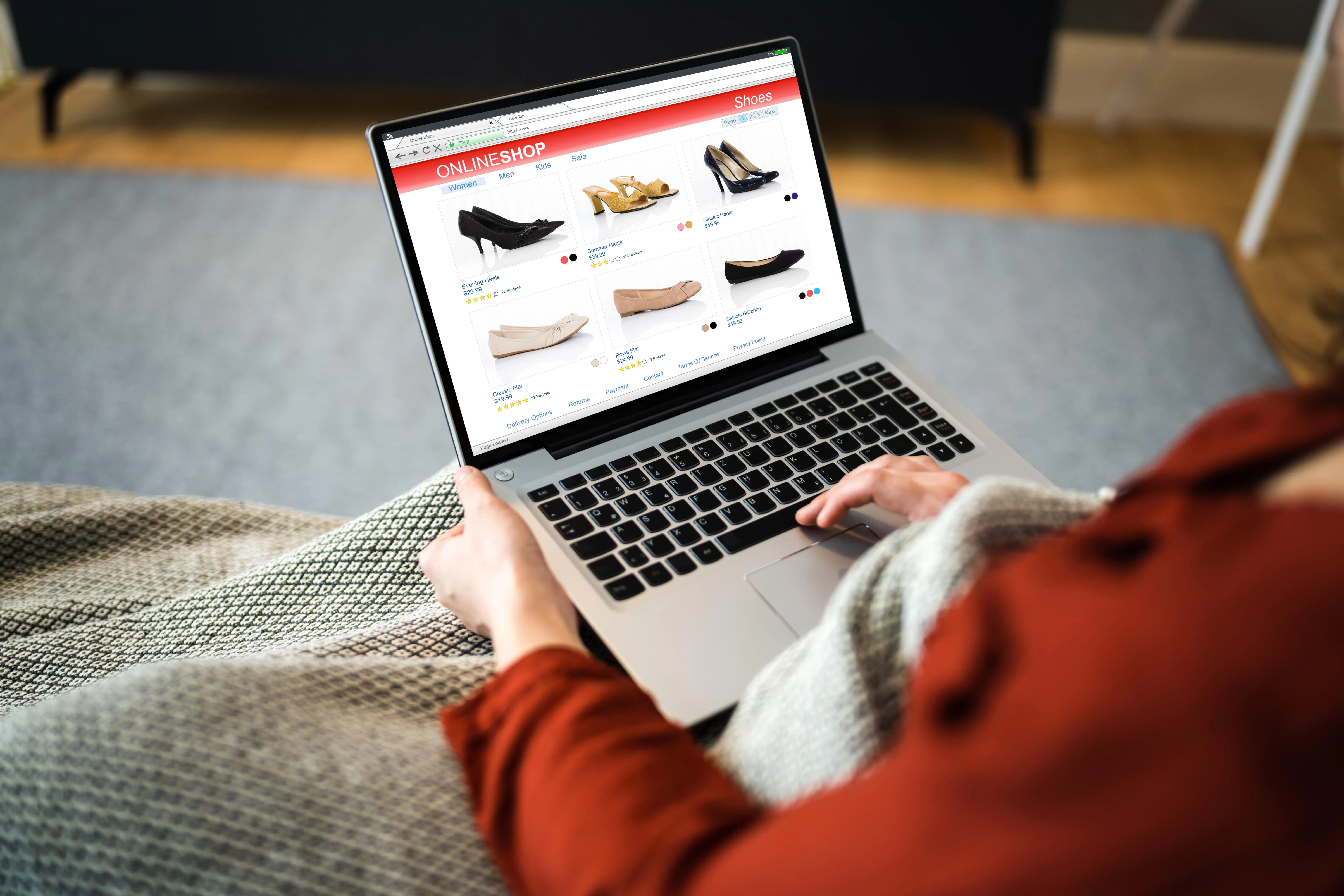 Person sitzt mit Laptop auf dem Schoß und besucht einen Online-Shop für Damenschuhe.