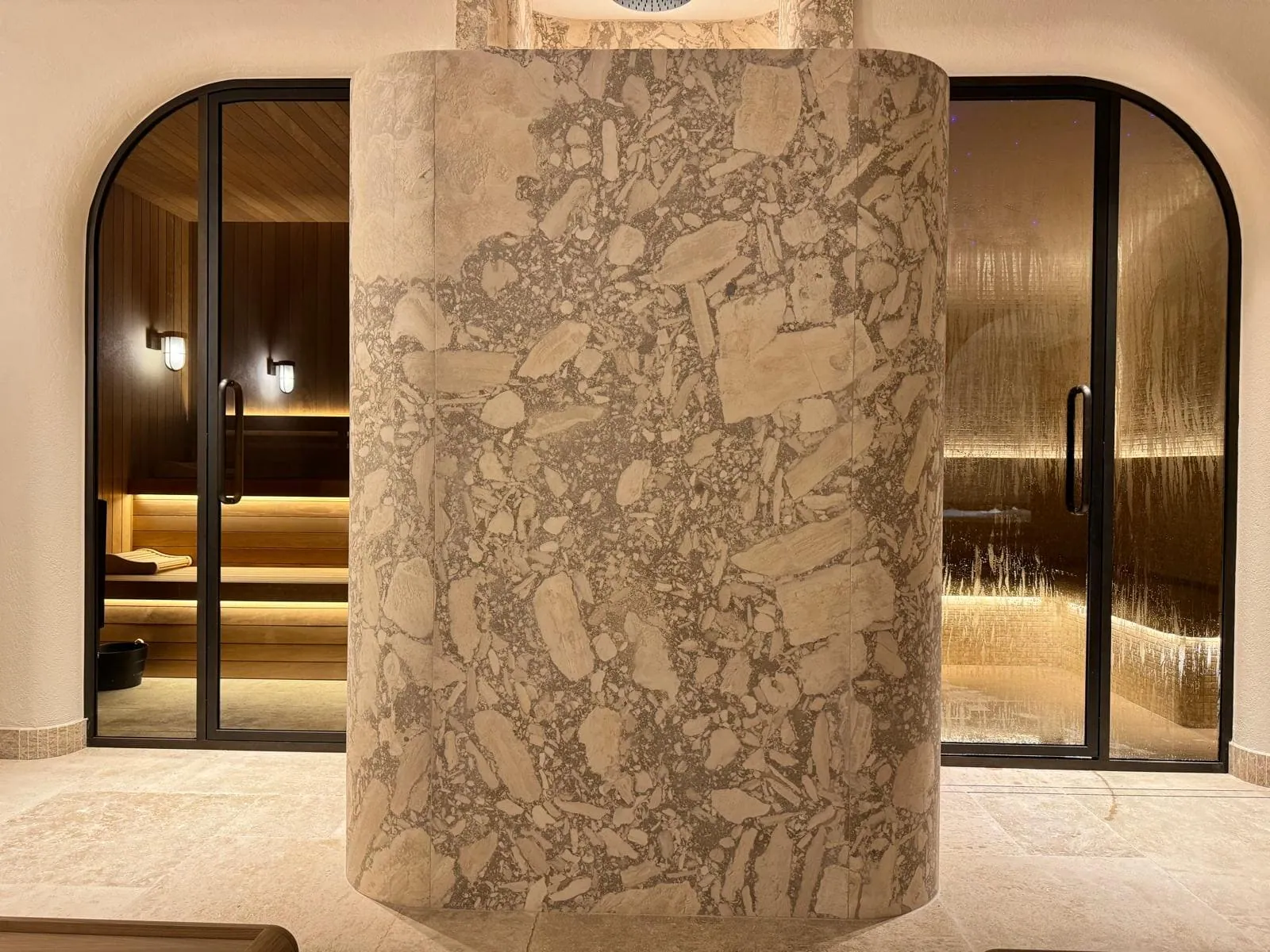 Pièce bien-être avec sauna vitré, douche et pierre naturelle réalisée par Nöje