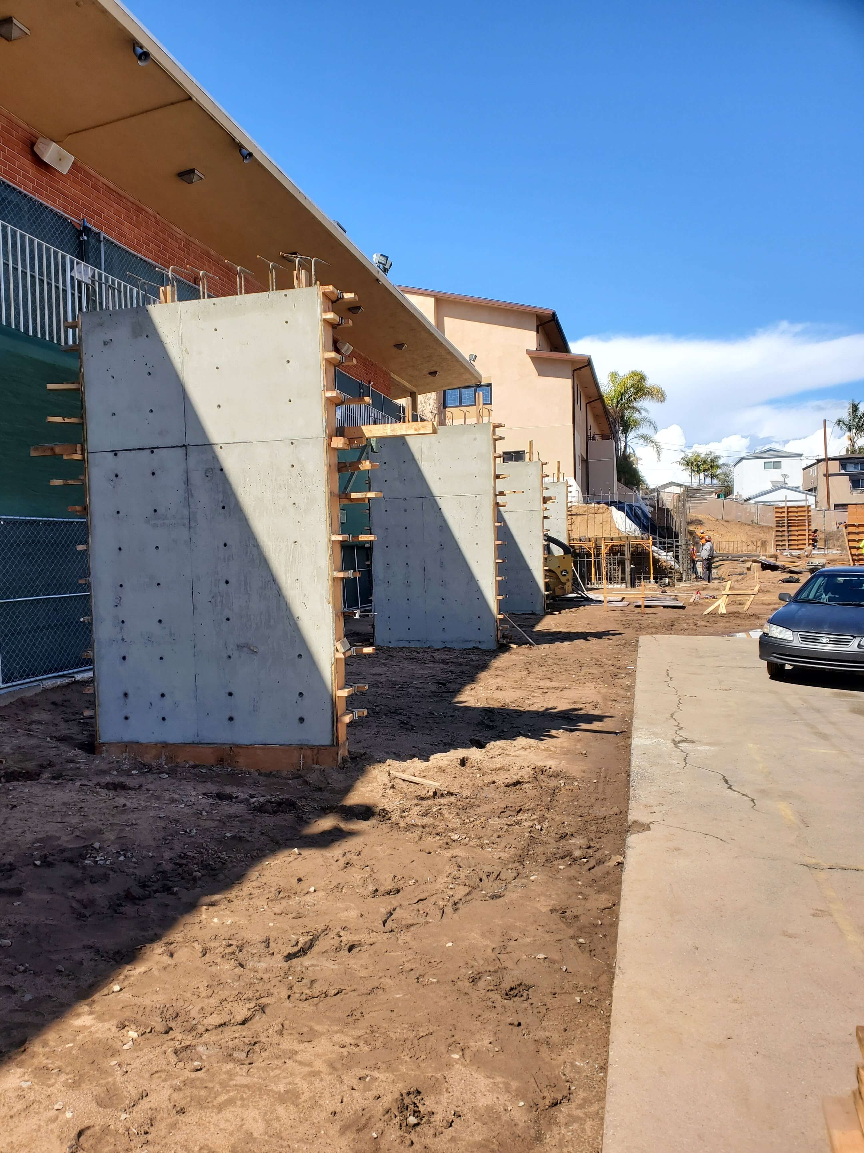 Construction site with multiple large concrete formwork panels aligned near a building and workers in the background.