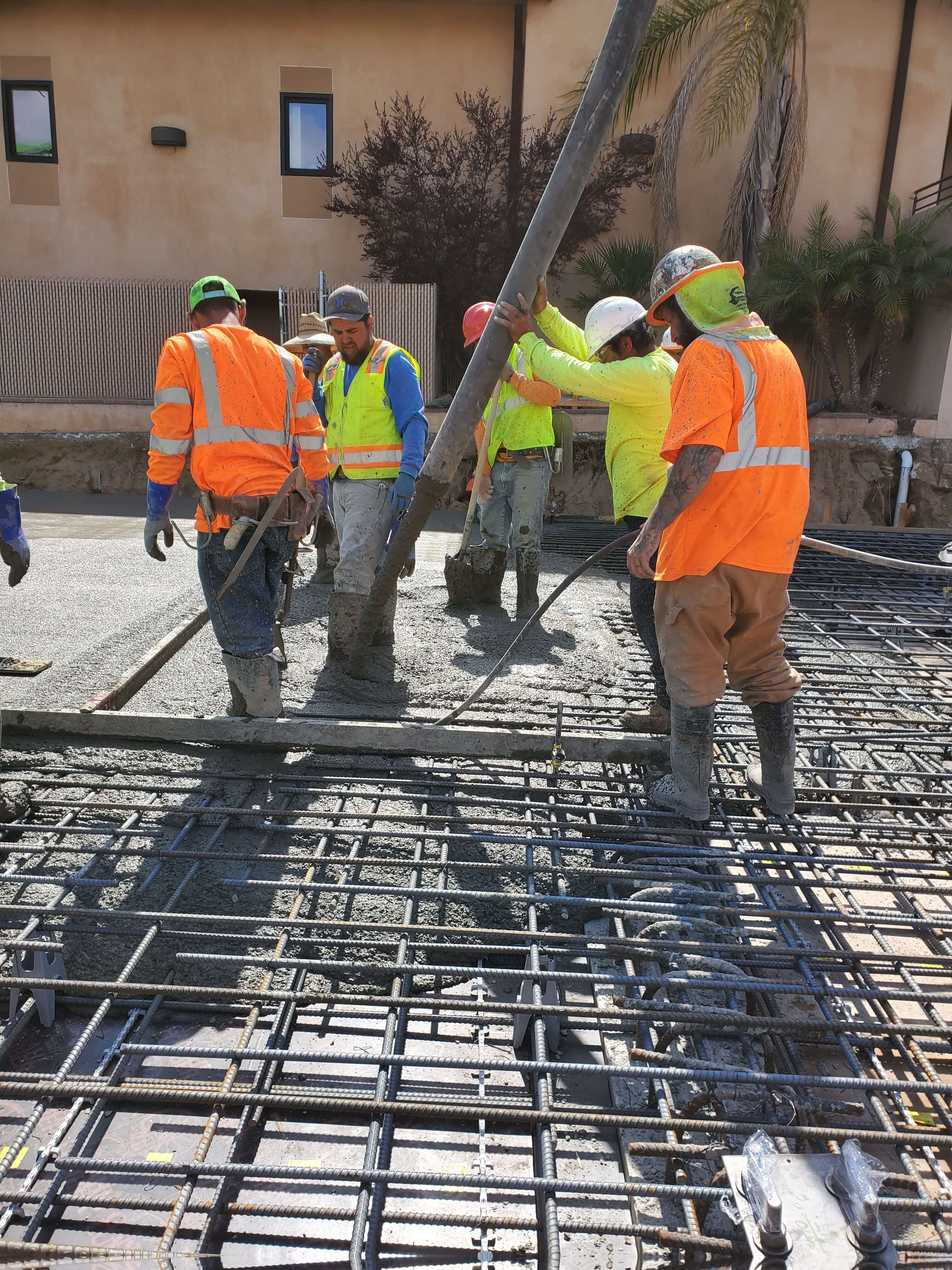 Construction workers in safety vests and helmets pouring concrete over steel rebar on a building site.