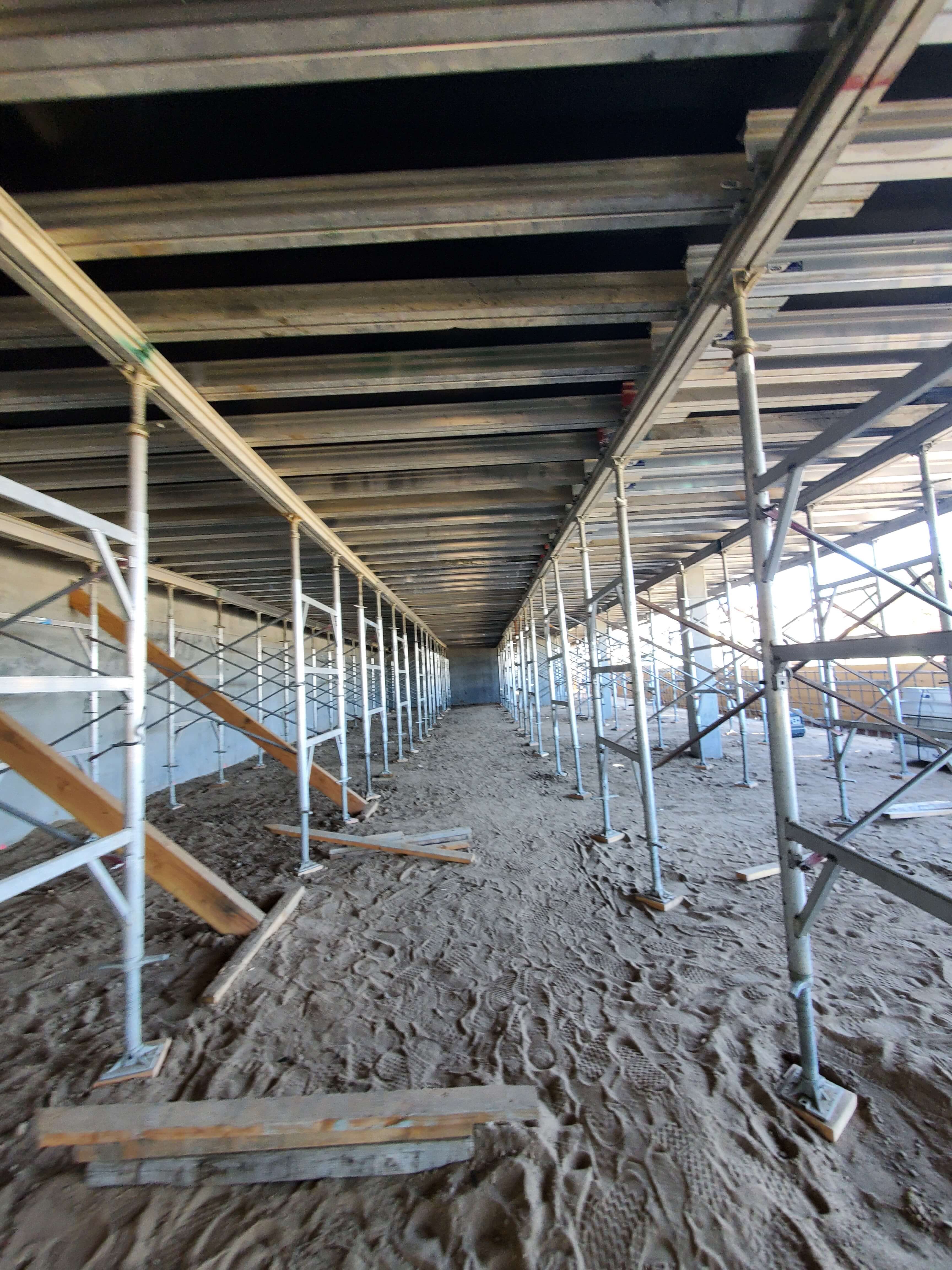 Under construction area with scaffolding supporting a ceiling and sandy ground with footprints.