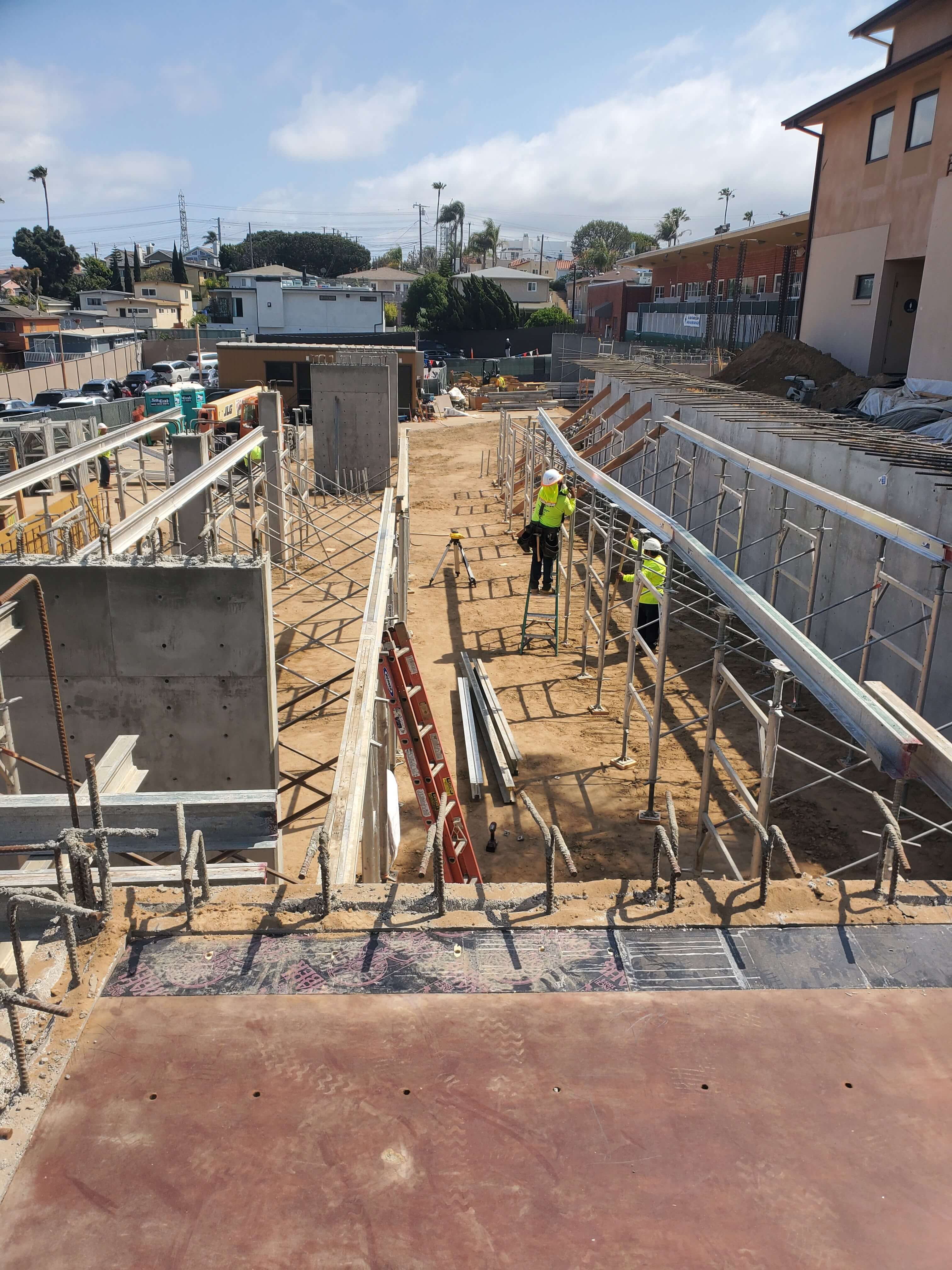Construction site with two workers in yellow safety jackets assembling scaffolding on a sunny day.