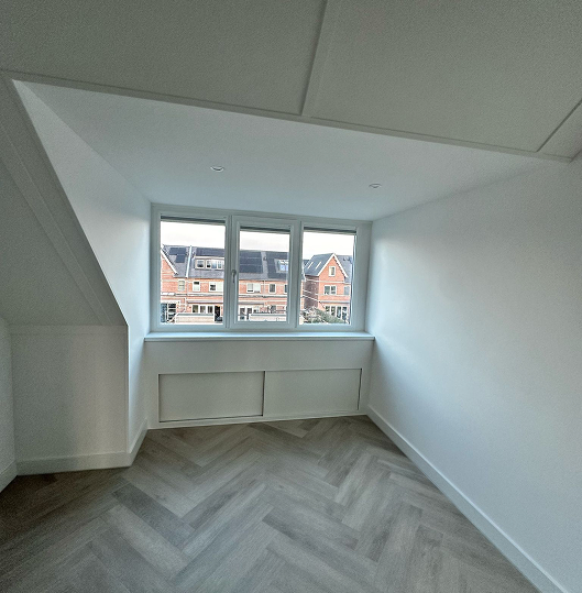 Modern dining area with a wooden table featuring a black glass top, surrounded by dark purple chairs and a wall with vertical wood paneling, adjacent to a doorway leading to a bedroom.