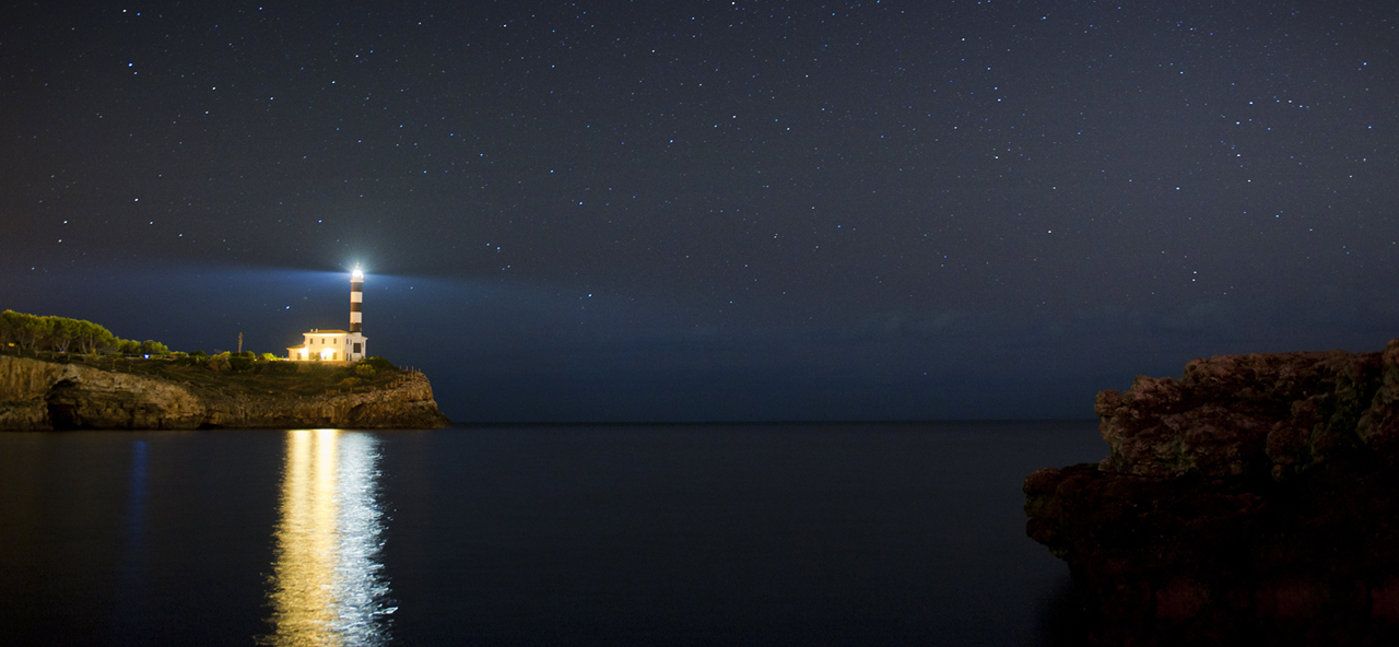 Website background image for hero banner - lighthouse lit at night, on the water