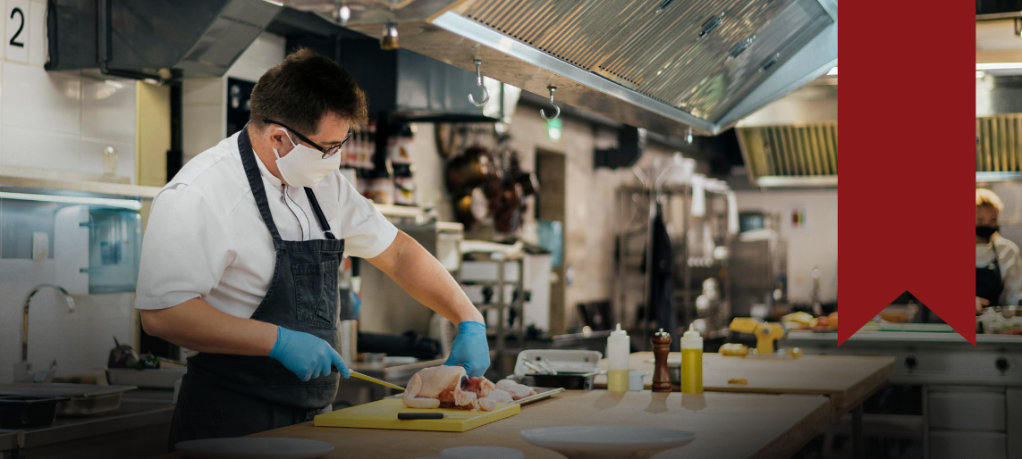 Chef wearing a mask and gloves preparing food in a commercial kitchen.