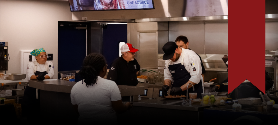Chefs working and demonstrating food preparation inside a commercial test kitchen.