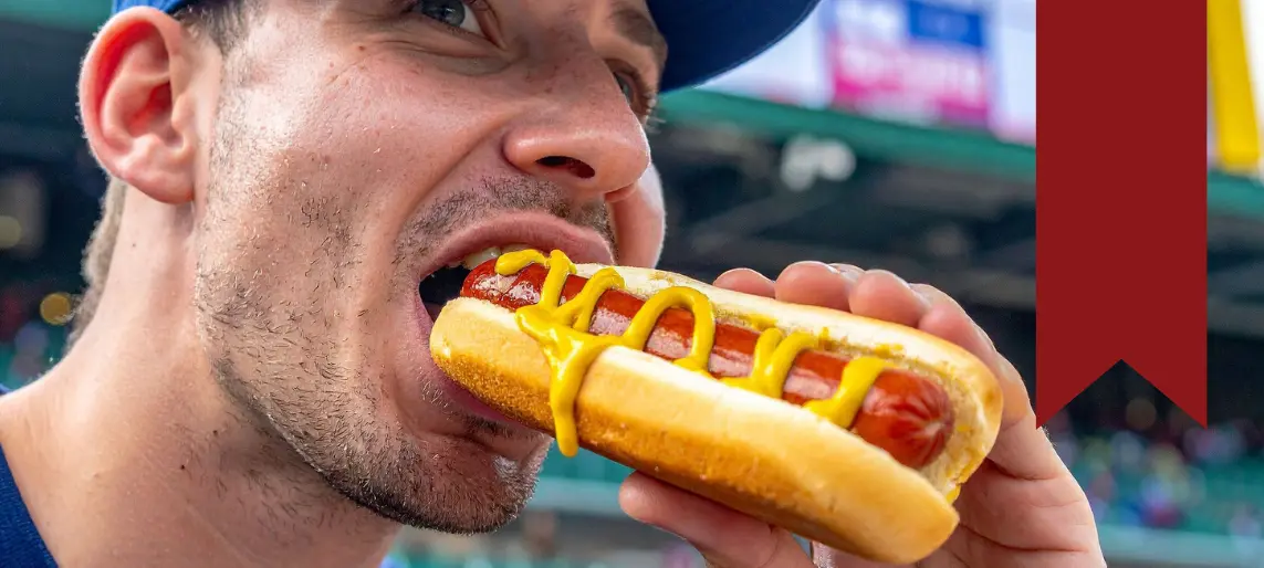 Customer eating a hot dog with mustard at a stadium concession stand.
