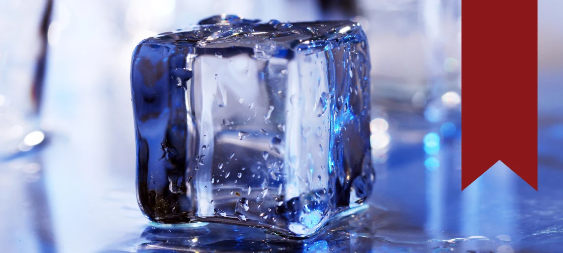 Close-up of a clear ice cube on a reflective surface, highlighting ice clarity and quality.