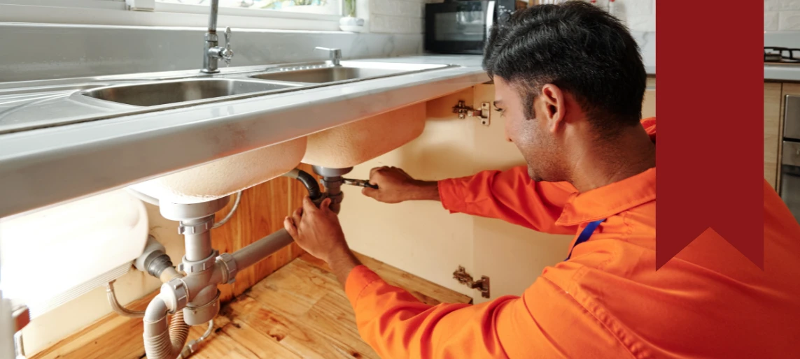 Technician repairing plumbing connections under a commercial kitchen sink