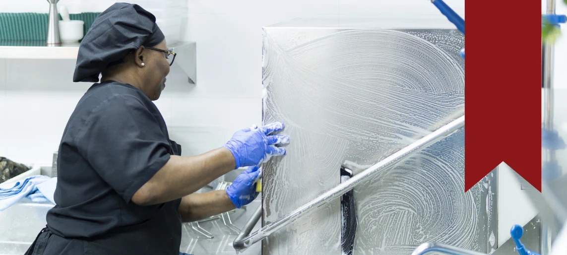 Foodservice worker cleaning and sanitizing commercial kitchen equipment during routine maintenance.