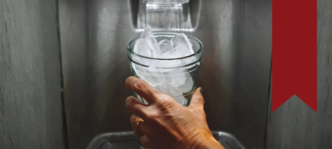 Hand filling a glass with ice from a commercial ice machine dispenser, highlighting common ice machine use