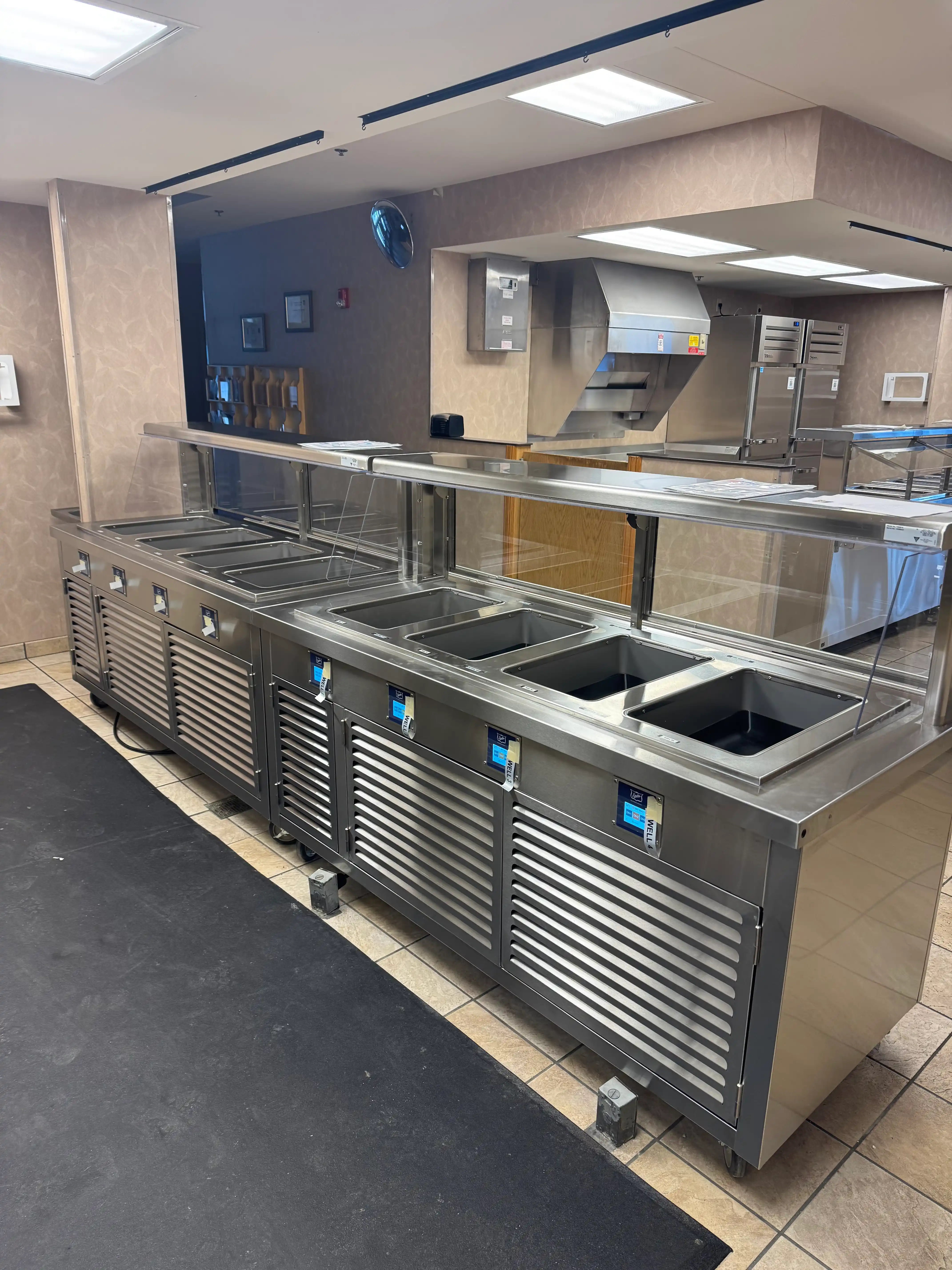 Stainless serving line with refrigerated prep wells and sneeze guard.