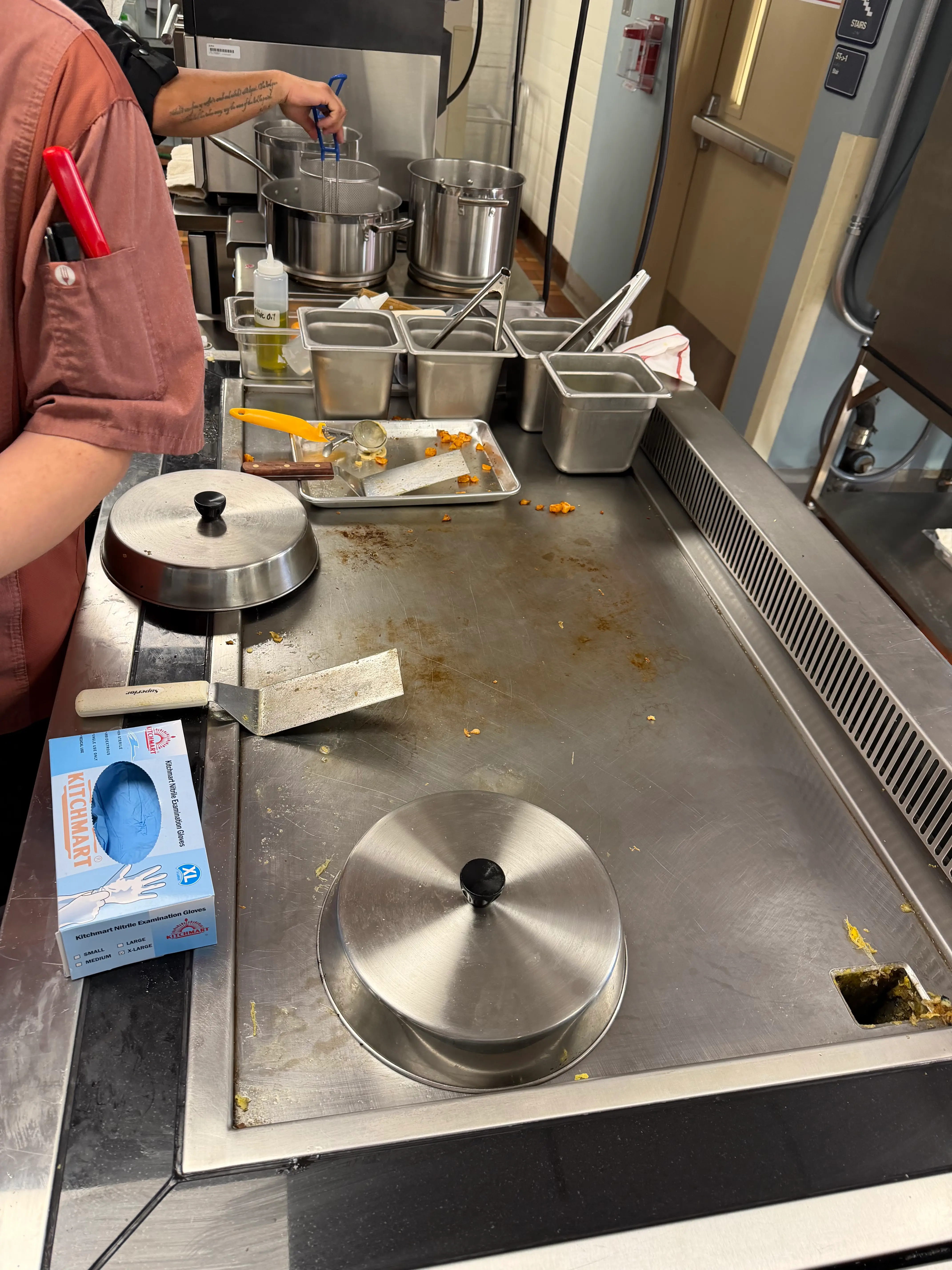 Commercial kitchen stovetop with pots, utensils, and prep containers during cooking.