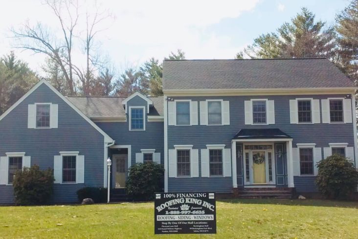 Blue house with white trim and a new dark roof, with a roofing king company sign in front.