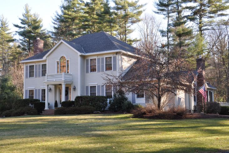 Elegant two-story house with a dark roof surrounded by trees.