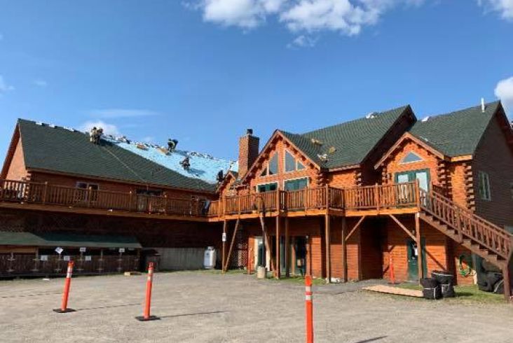 Large wood cabin with blue tarp covering part of the roof under construction.