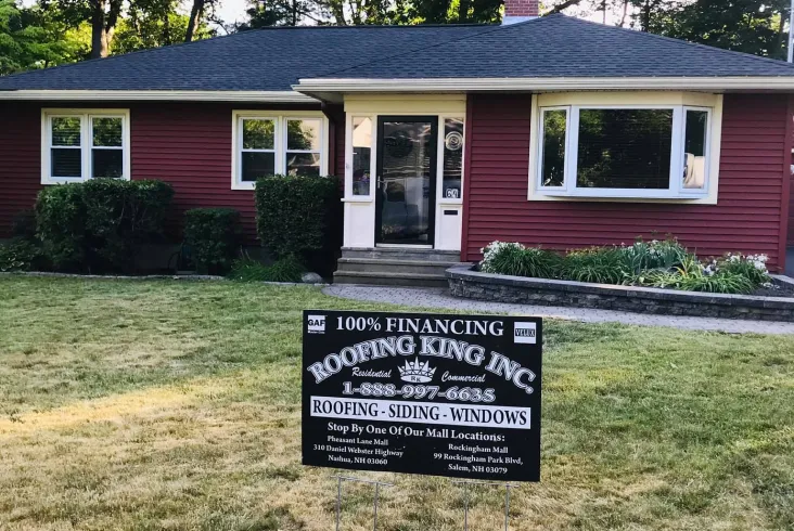 Single-story red house with a Roofing King sign on the lawn.