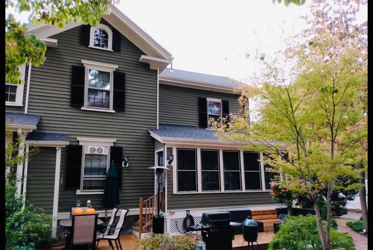 Back view of a green house with a spacious patio and trees.