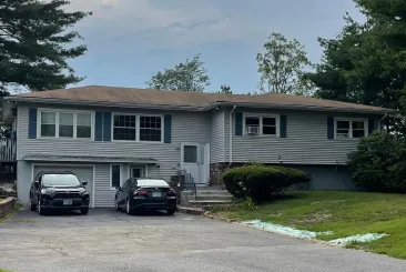 Blue house with white trim and a new dark roof, with a roofing king company sign in front.