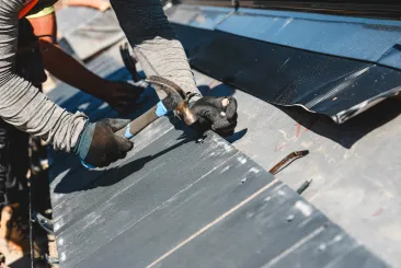 Roofer using a hammer on a metal roof in Gloucester, MA.