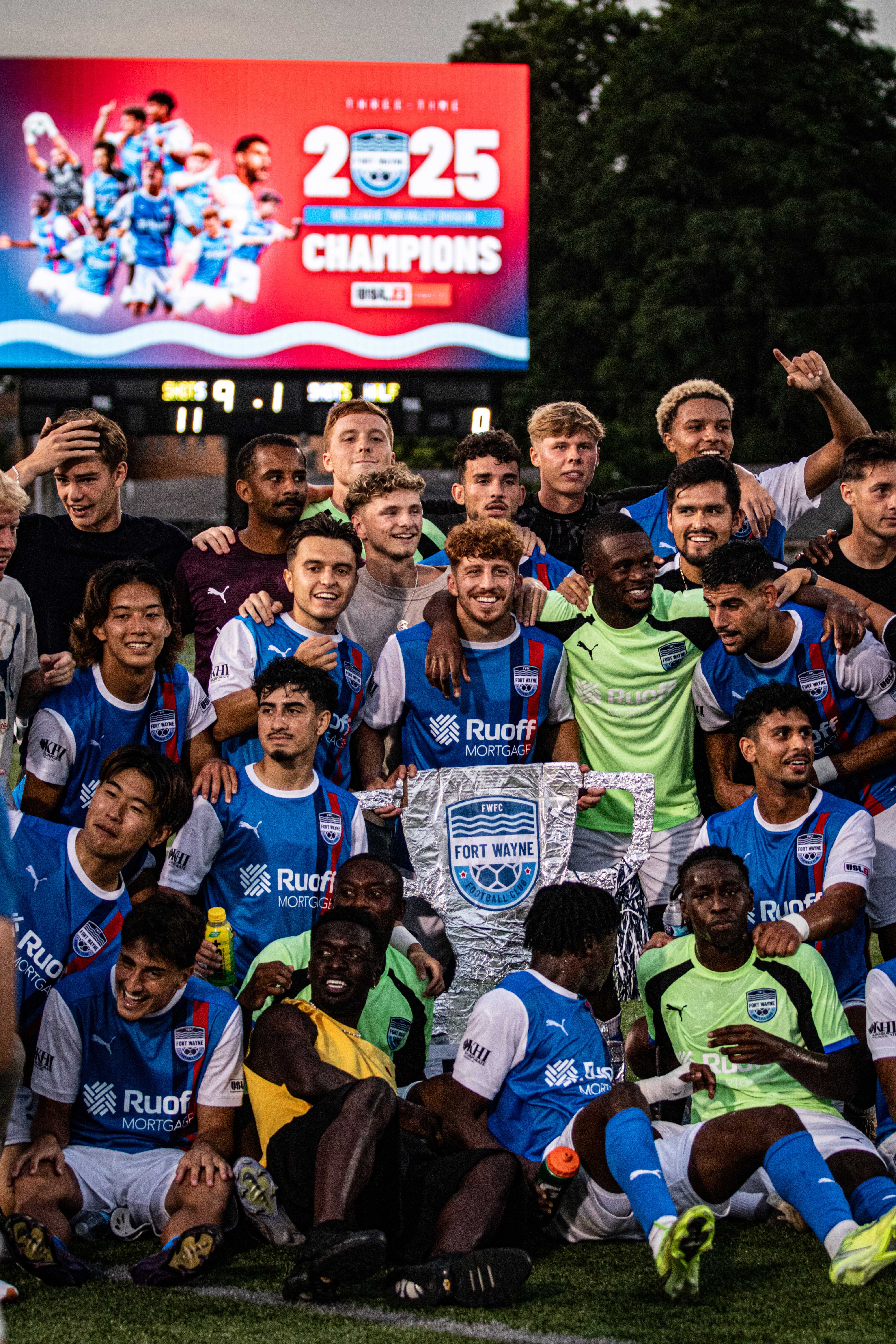 A group photo of Fort Wayne FC posing with a fan-made trophy.