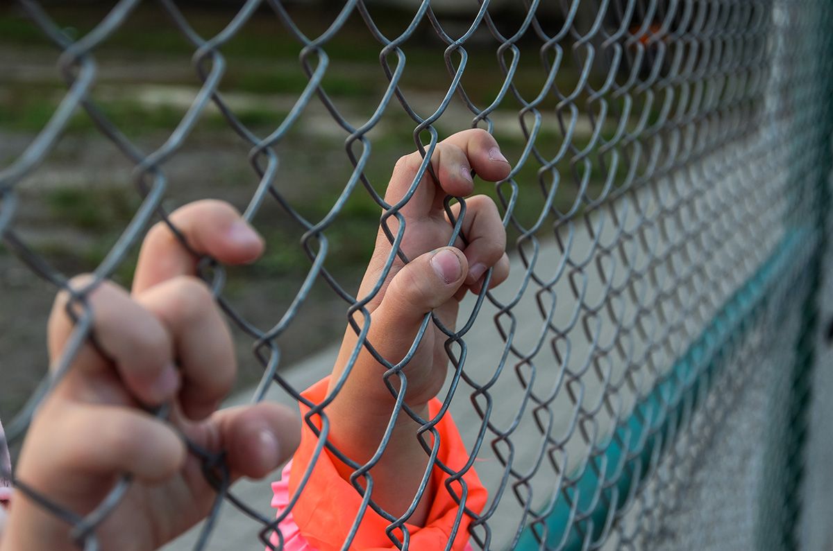 A person is holding onto a chain link fence with their hands.