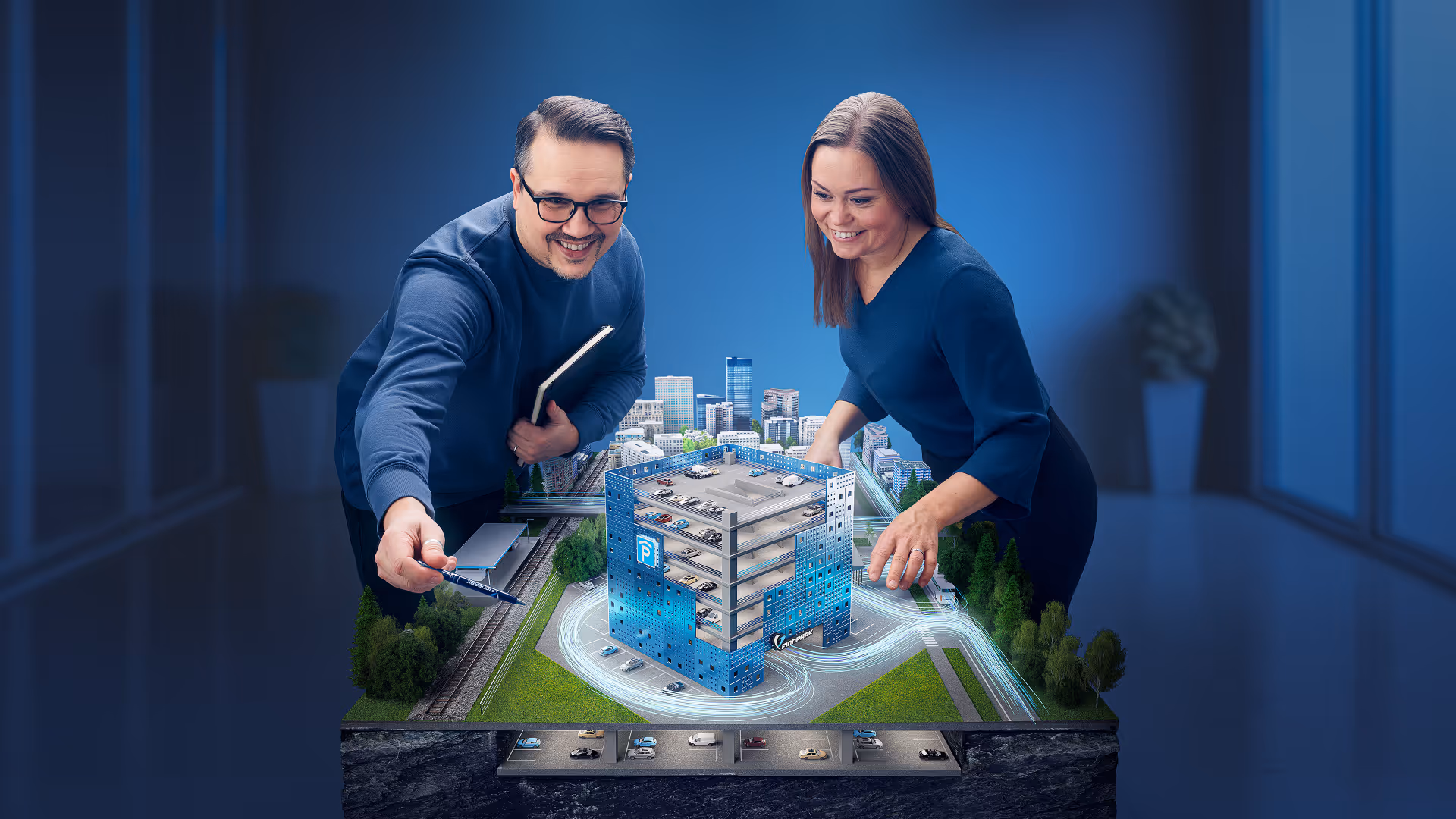 Mies ja nainen tutkailevat pienoismallia kerrostalosta, jonka ympärillä on kulkevia valoviivoja.
