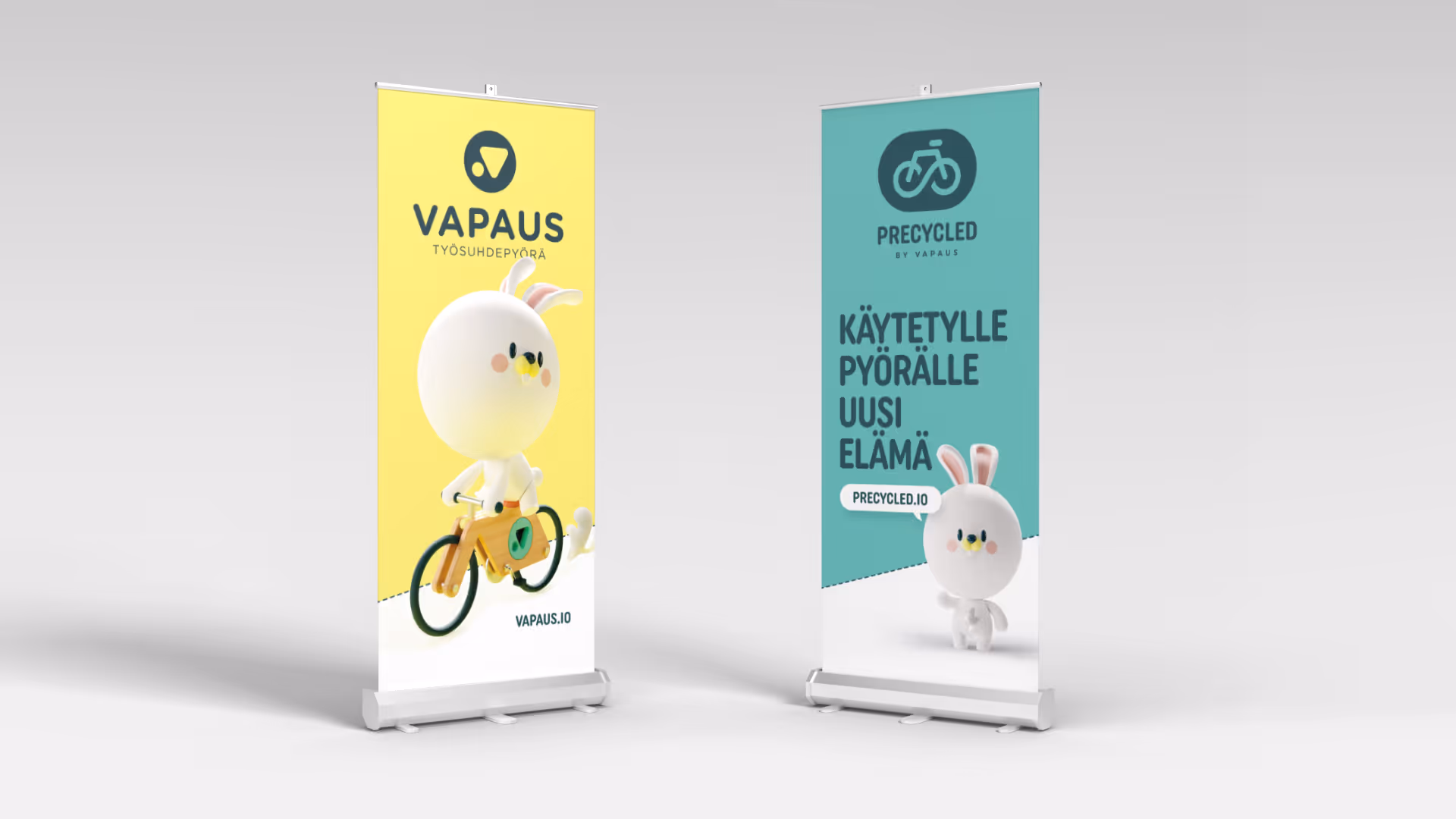 Kaksi roll-up-mainosta, vasemmassa hahmo ajaa pyörää ja oikeassa hahmo seisoo kara, tekstit suomeksi.