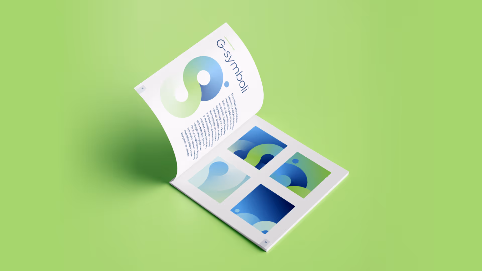 A booklet open on a green surface showing a large G-symboli logo on the left page and four smaller colorful abstract square designs on the right page.